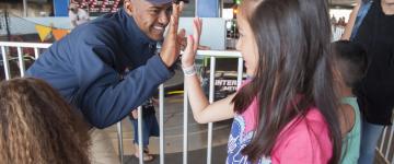 A Santa Cruz Beach Boardwalk employee high-fives a young guest waiting in line for bumper cars attraction