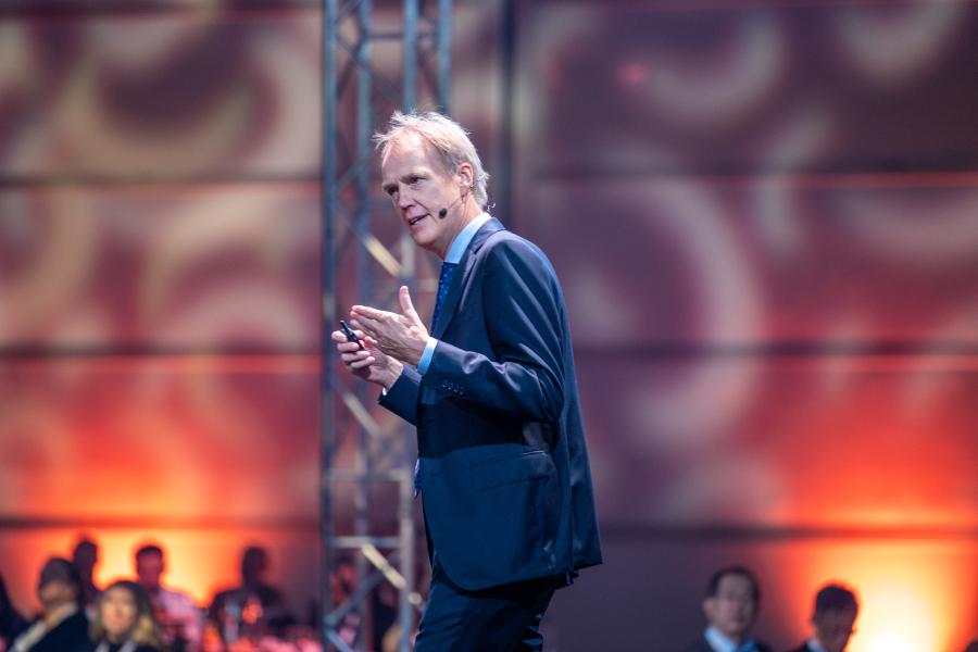 Man with gray hair walking on stage speaking to professionals