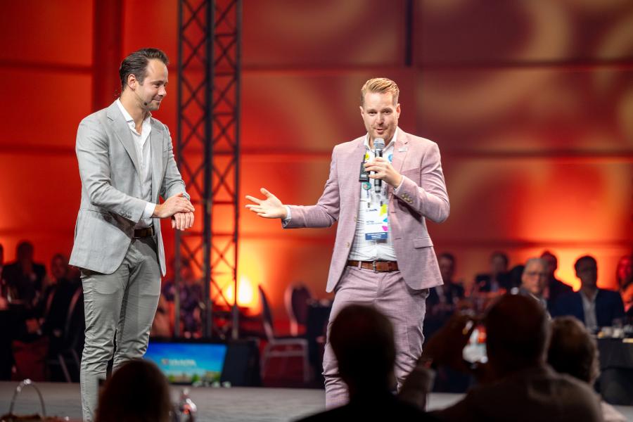 Two men on stage speaking to professionals 