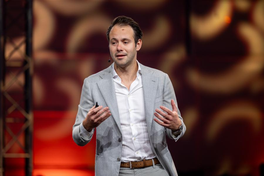 dark haired man on stage speaking to professionals as they eat breakfast.