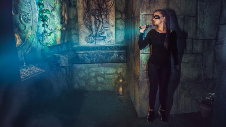 Illustrative concept art of a woman with a black eye mask and bodysuit, shining a flashlight on the left side of the image with visible tomb.