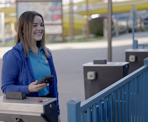 An amusement park employee smiling and holding a smartphone with a mobile scanner to scan ticket entry